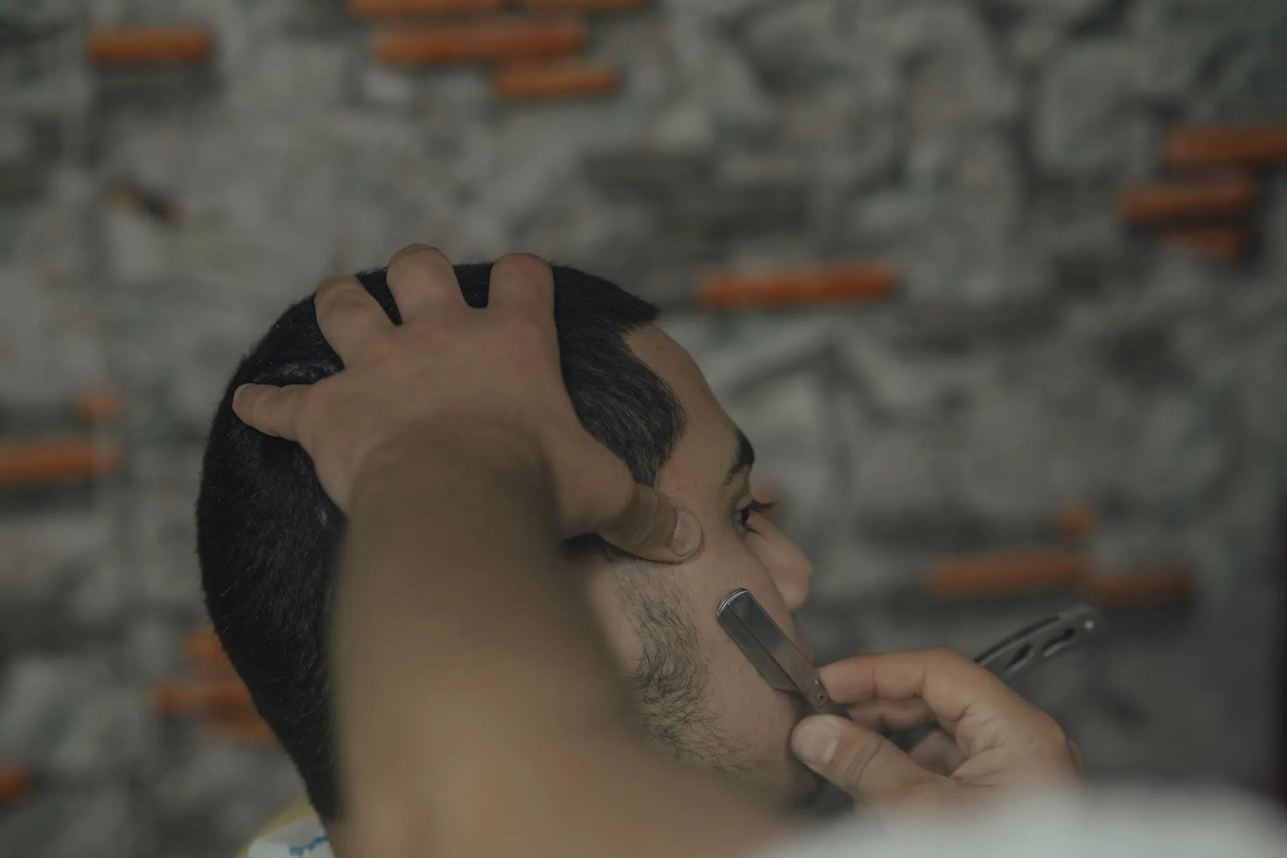 Detail rukou barbera tvořícího vlasový vzor na hlavě klienta